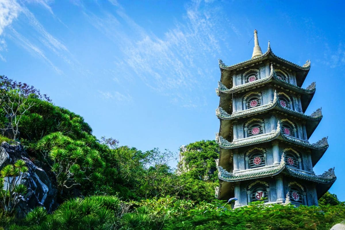 Ancient multi-tiered Buddhist pagoda with ornate green curved roofs and circular windows surrounded by lush tropical vegetati