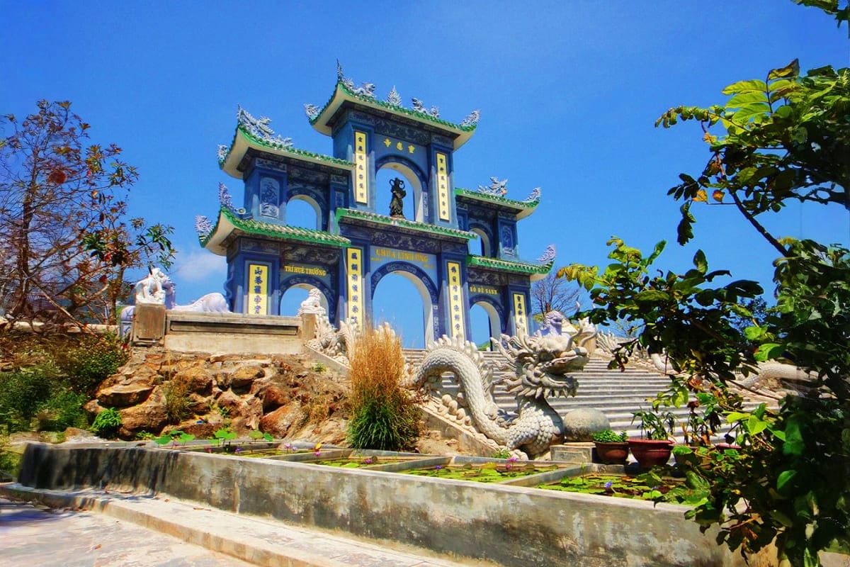 Traditional Vietnamese temple gate with blue and green tiered roofs, ornate dragon sculptures, and stone steps against clear 
