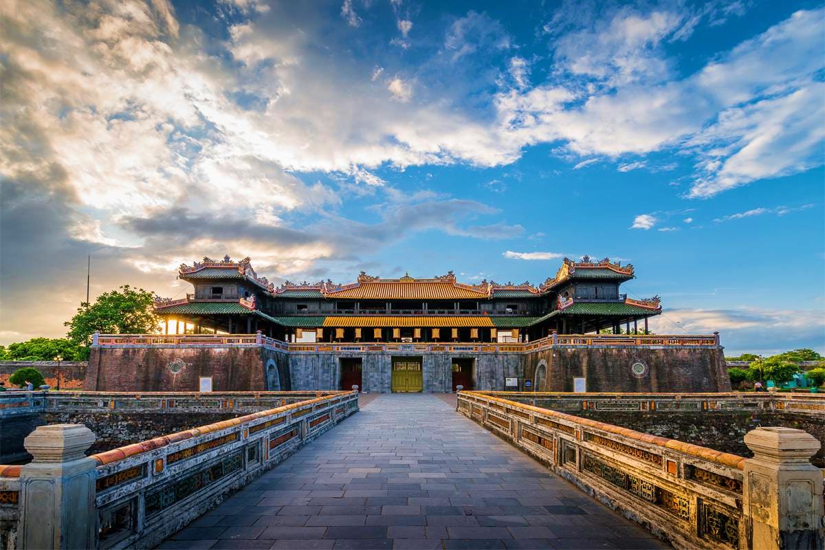 Ancient Vietnamese imperial citadel with traditional yellow-tiled roofs, stone walls, and ceremonial gates under blue sky wit