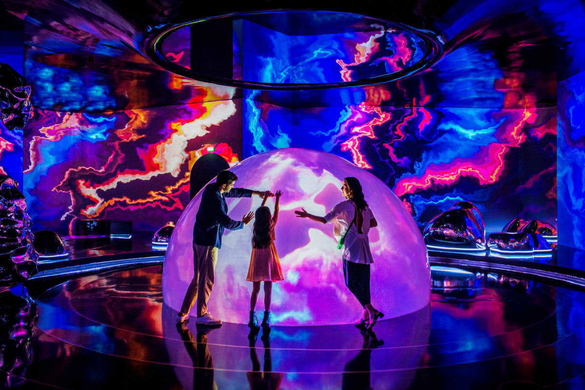 Family exploring interactive digital dome with colorful neon light displays and projection mapping at AYA Universe immersive 