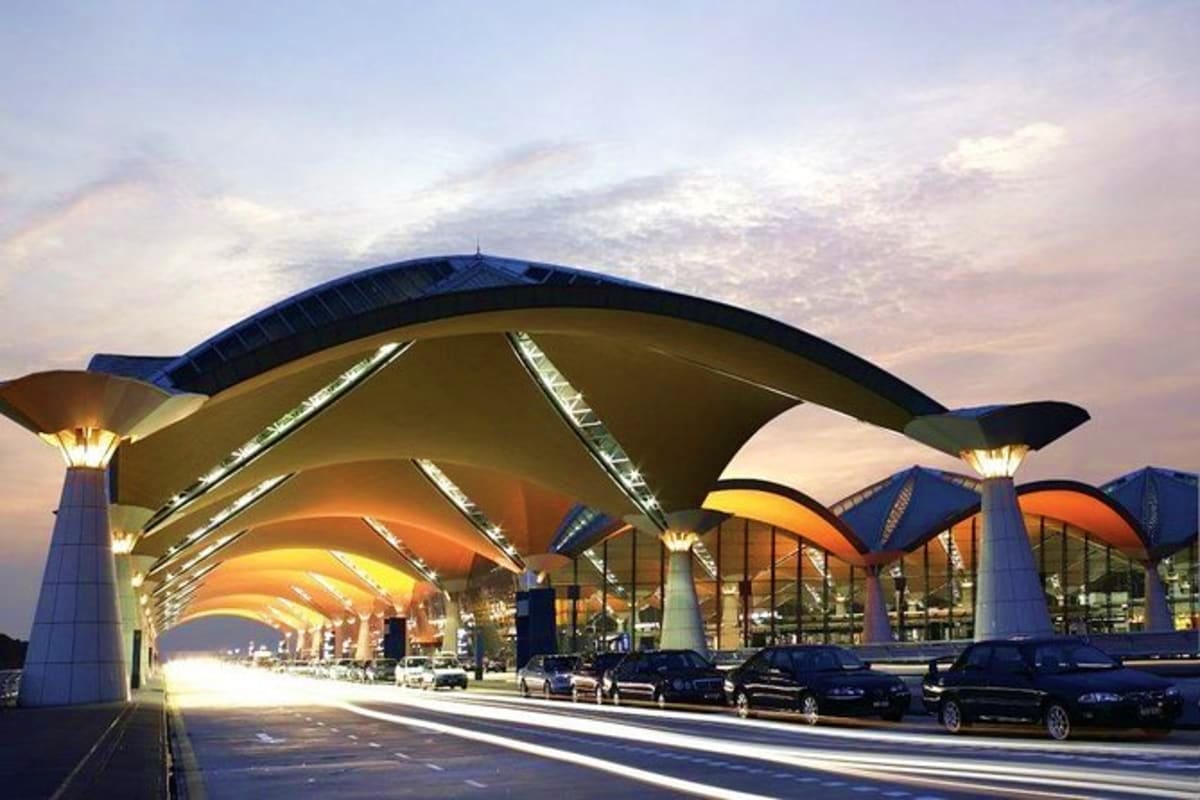 Modern airport terminal with curved architectural design and parked vehicles under illuminated canopy at dusk