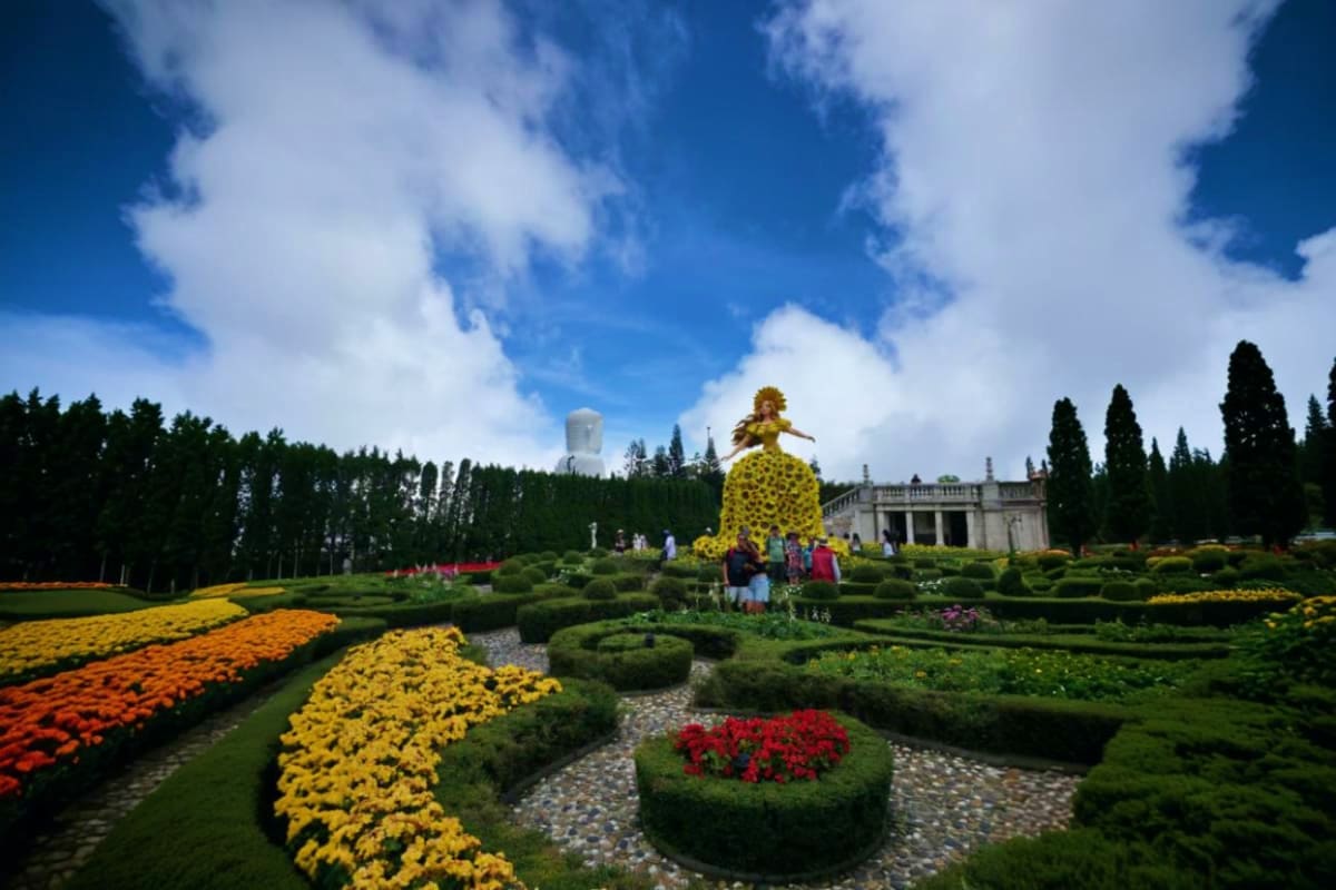 Formal garden at Ba Na Hills featuring colorful flower beds, manicured hedges, giant golden chicken sculpture, and classical 