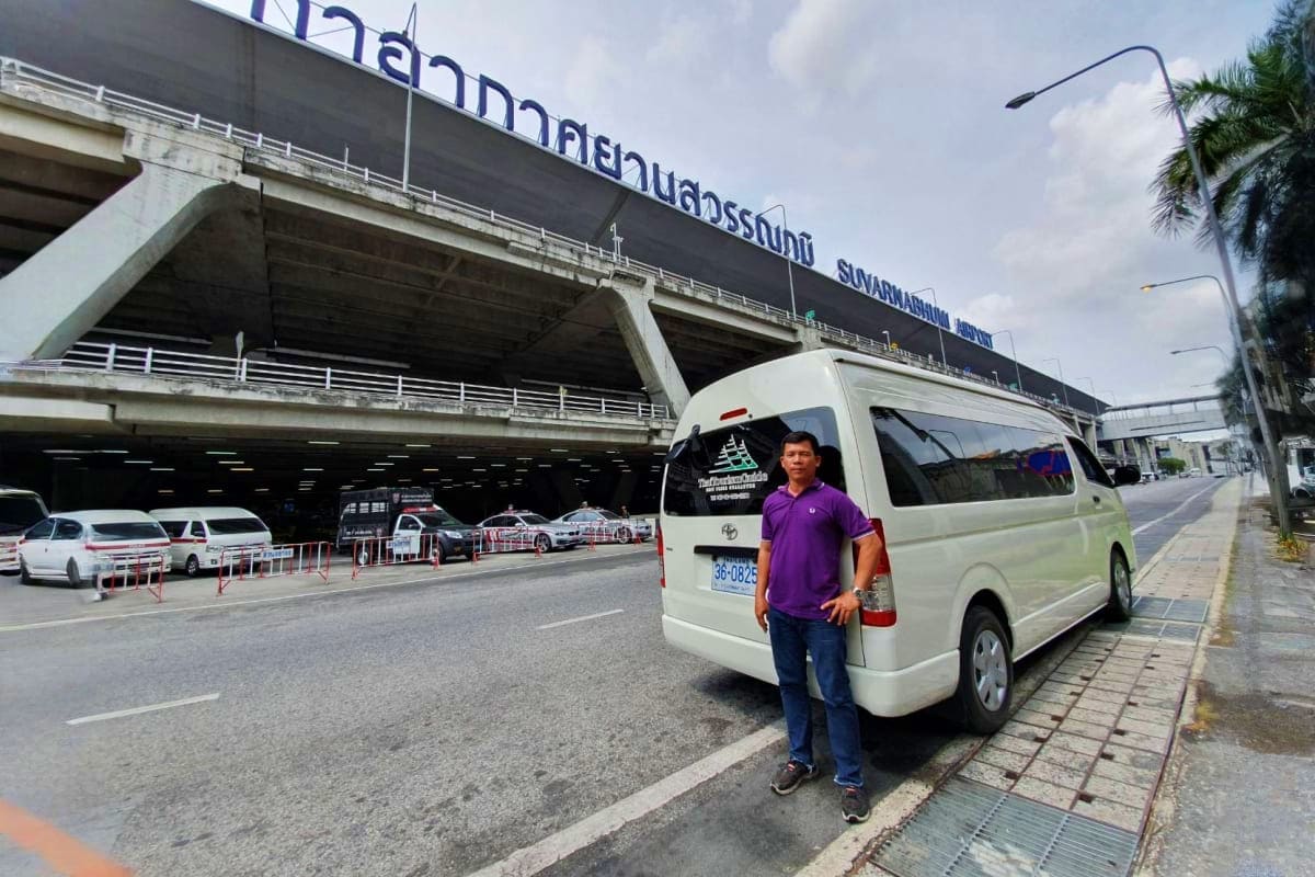 Man standing beside white Toyota van at Suvarnabhumi Airport entrance with pickup service vehicles parked underneath