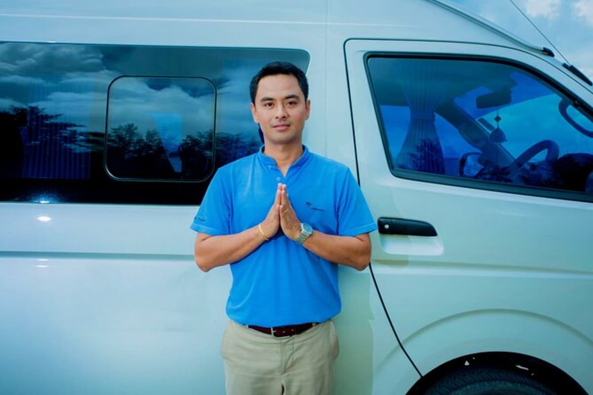 Man in blue shirt making welcome gesture in front of white van for airport transfer service