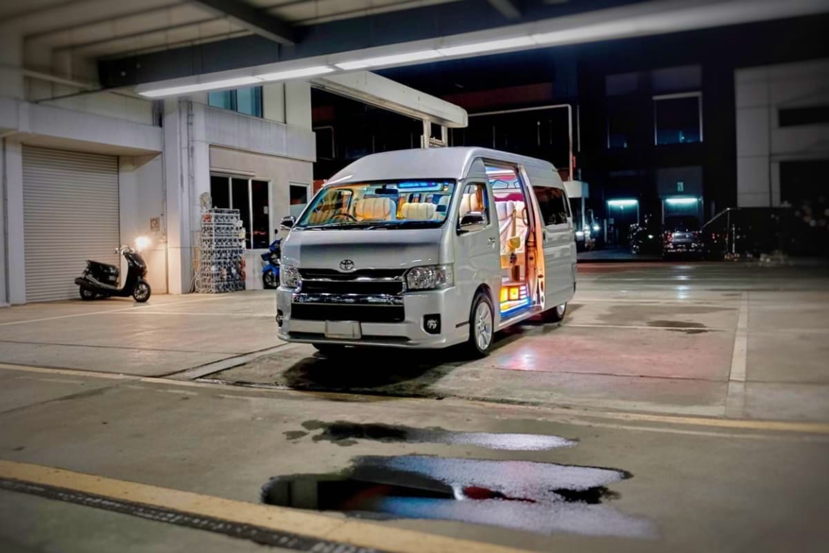 White Toyota van with open sliding door parked at night in covered parking area, showing interior seating for hotel transfer 