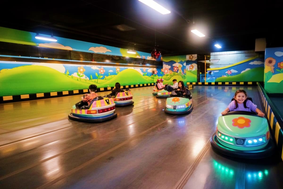 Children riding colorful bumper cars in a brightly lit indoor arena at Berjaya Times Square Theme Park with whimsical wall mu