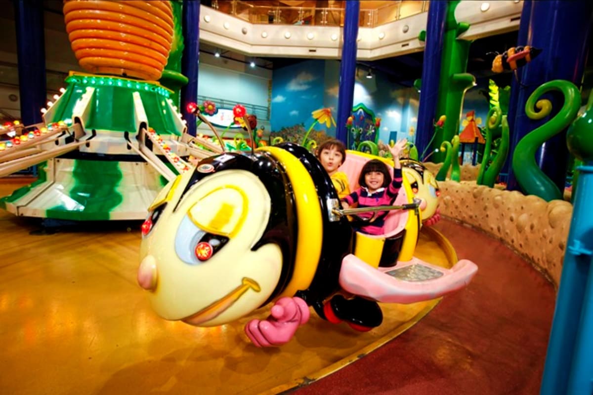 Children riding a colorful bee-themed ride at Berjaya Times Square Theme Park indoor attraction with vibrant green decorative