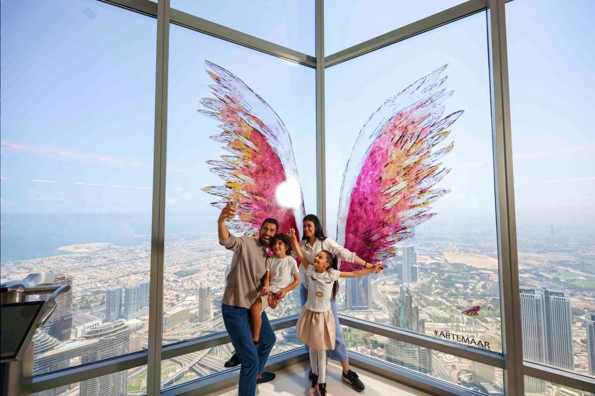 Family of four posing with colorful wing art installation at high-altitude observation deck overlooking Dubai cityscape