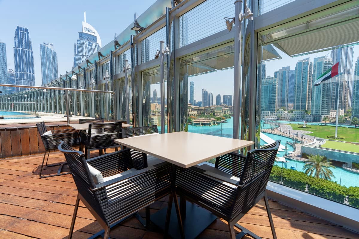 Rooftop dining area with panoramic views of Dubai skyline, Burj Khalifa, and turquoise water fountain below from high-rise re