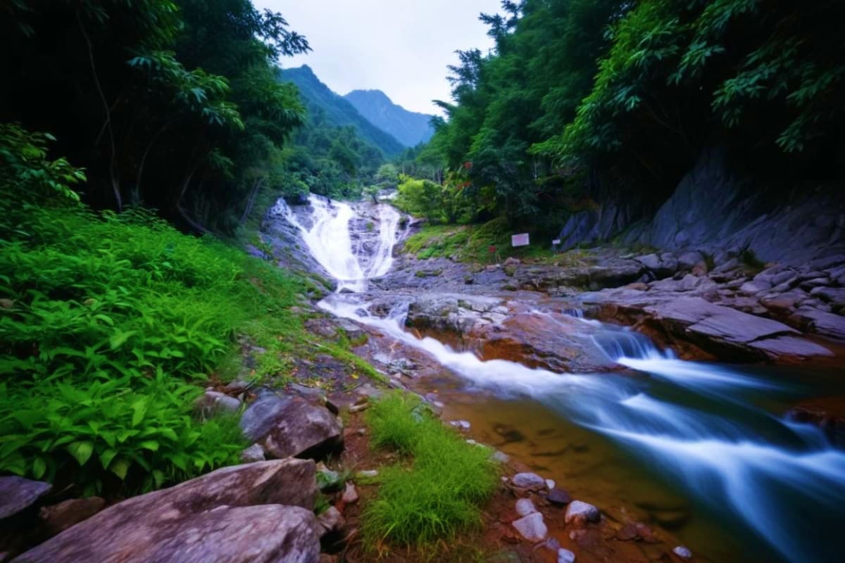 Cascading waterfall flowing through lush green forest valley with rocky stream and mountain peaks in Cameron Highlands