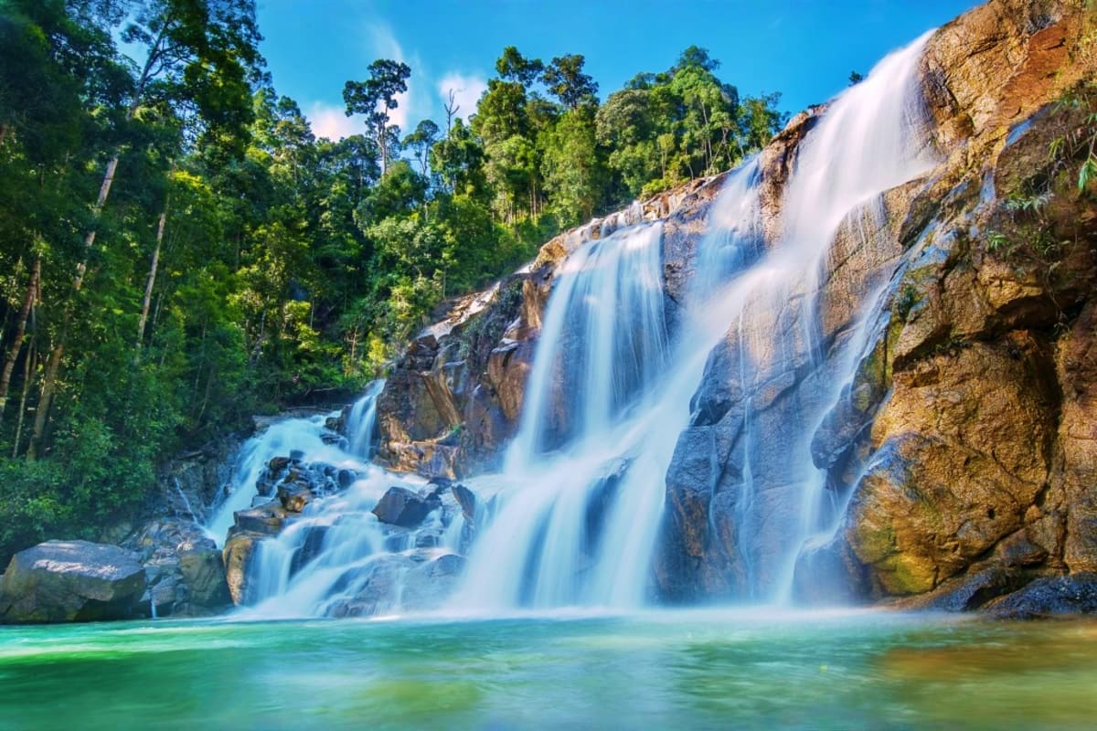 Cascading waterfall with turquoise pool surrounded by lush rainforest and rocky cliffs in Cameron Highlands