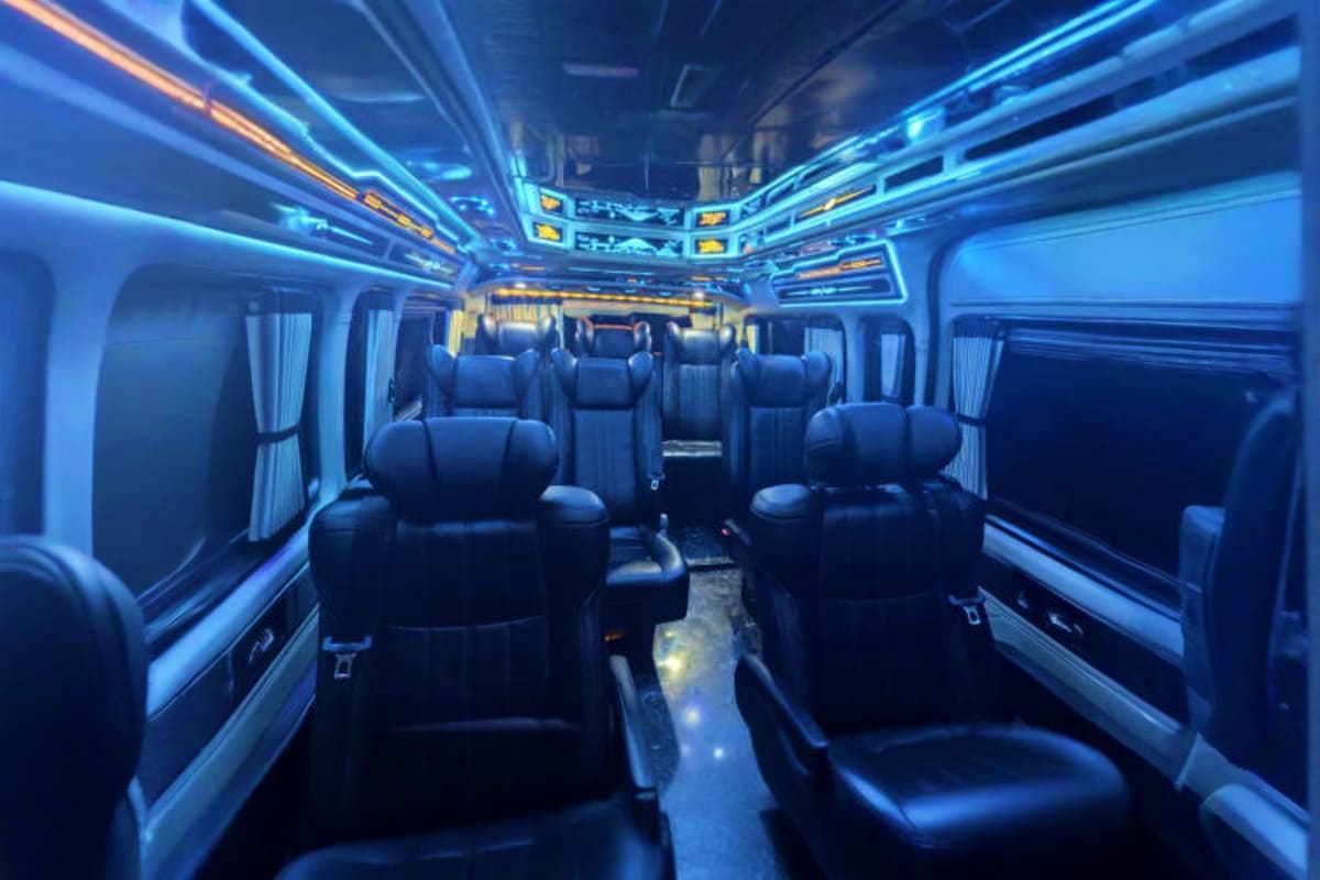 Luxury tour bus interior with black leather seats, blue ambient lighting, and large windows for airport transfer service