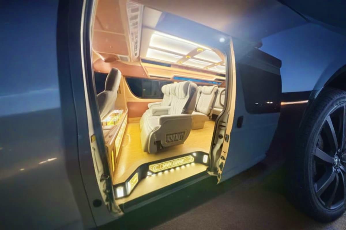 Open door of white van with beige interior seats and yellow floor lighting at night, ready for airport pickup service
