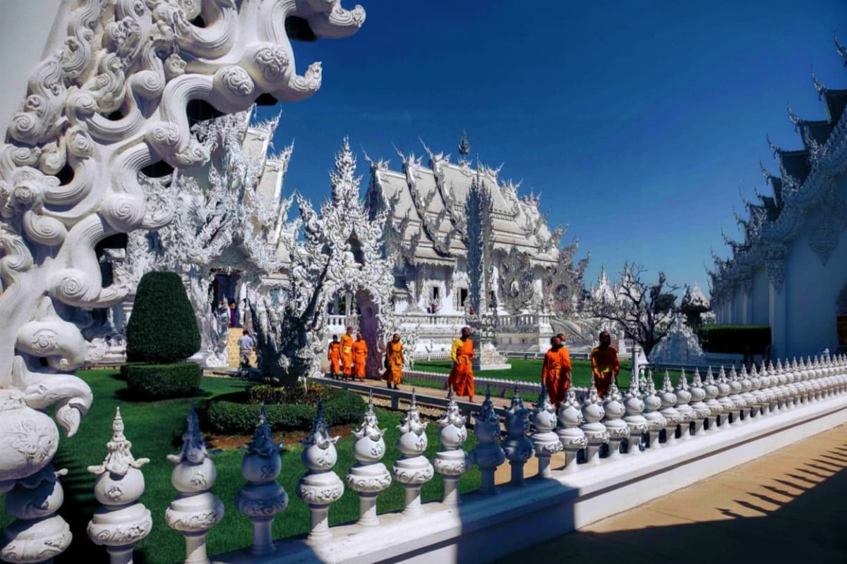 Buddhist monks in saffron robes walking through the ornate white temple grounds of Wat Rong Khun in Chiang Rai, Thailand