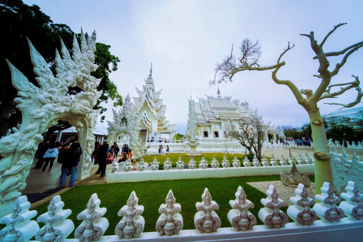 White Temple in Chiang Rai with ornate stone decorations, manicured grounds, and visitors exploring the iconic Buddhist shrin