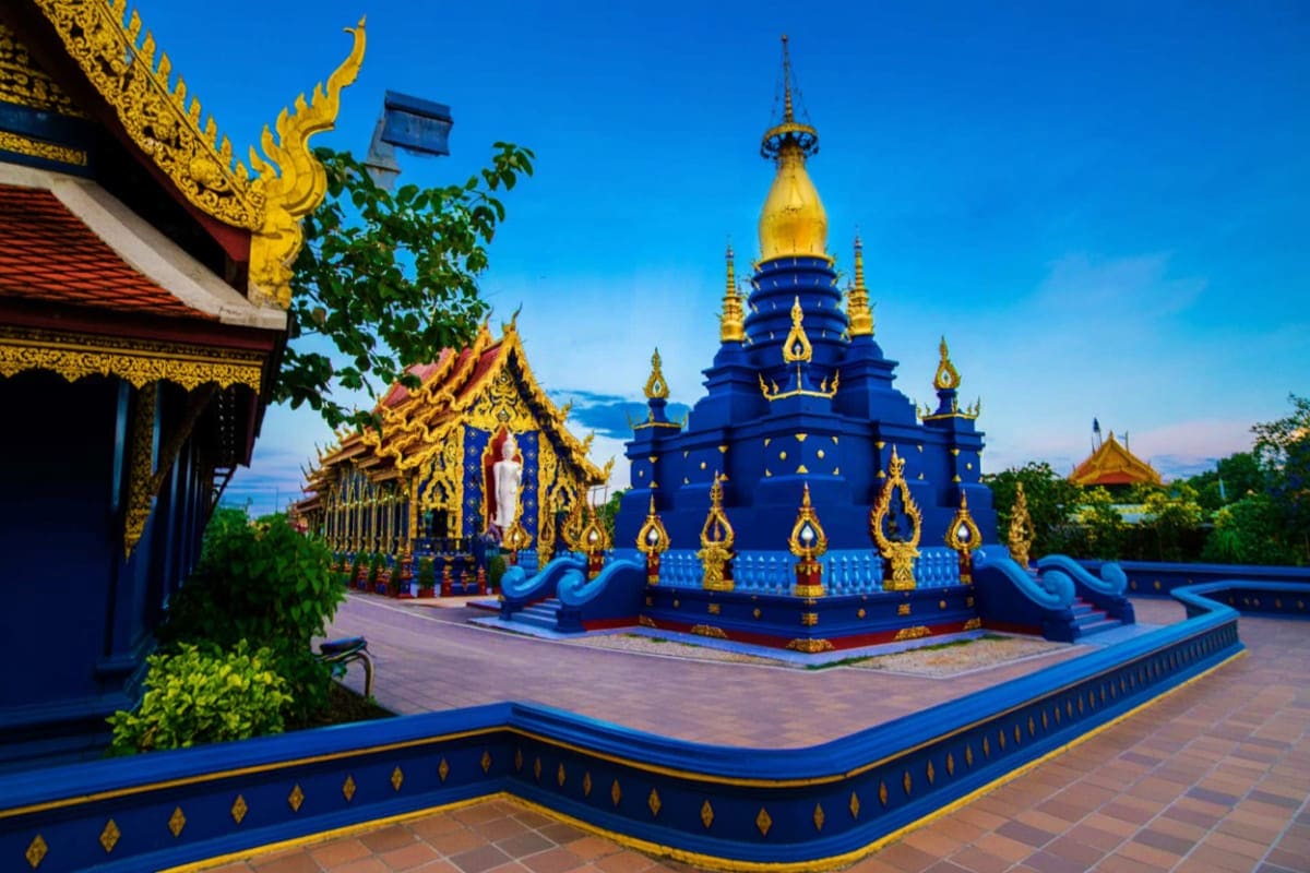 Blue temple with golden spires and ornate decorations in Chiang Rai, Thailand courtyard against clear sky