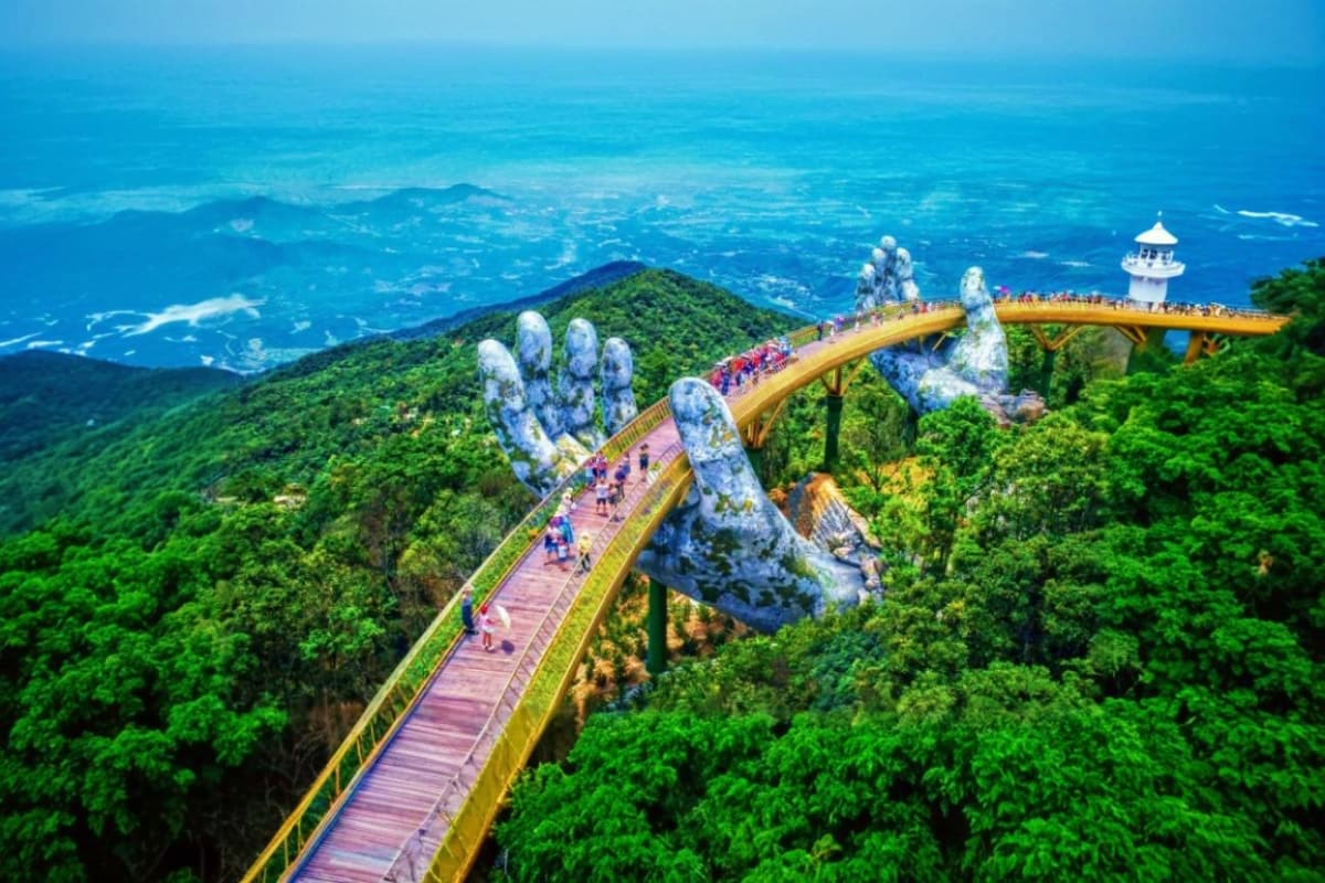 Golden Bridge with giant stone hands in lush green mountains overlooking blue ocean and coastline in Da Nang, Vietnam