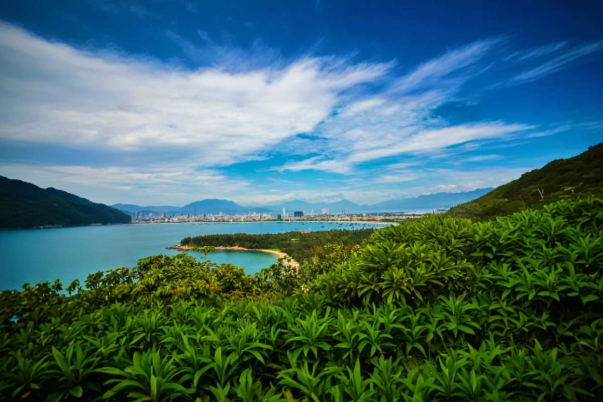 Scenic coastal view of Danang city skyline with turquoise bay waters, tropical vegetation, and mountains under blue sky