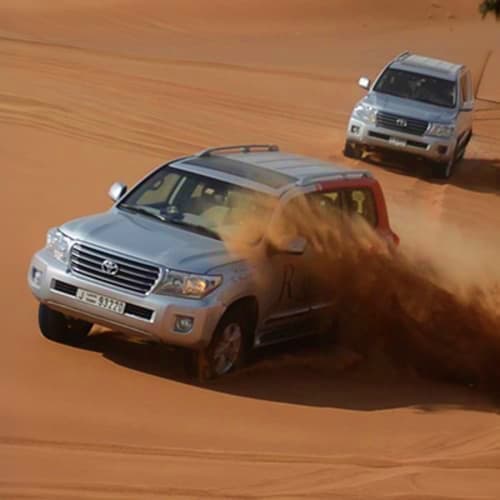 Two white Toyota SUVs driving on sandy desert creating dust clouds during a desert safari adventure in Abu Dhabi