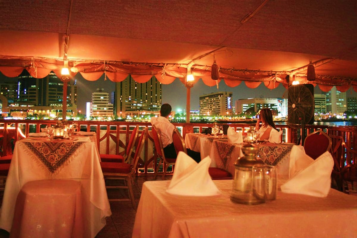 Elegant rooftop restaurant with white tablecloths overlooking illuminated Dubai cityscape at night
