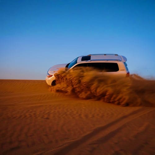 Dubai Desert Safari with Dune Bashing White SUV dune bashing through golden sand dunes creating dust clouds under clear blue sky in Dubai desert