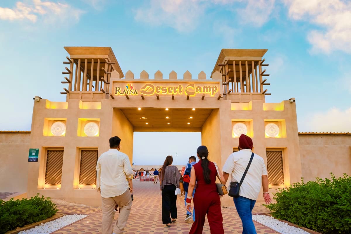 Dubai Desert Safari with Dune Bashing Visitors entering the illuminated gateway entrance of Rayna Desert Camp in Dubai at dusk with desert landscape visible beyond