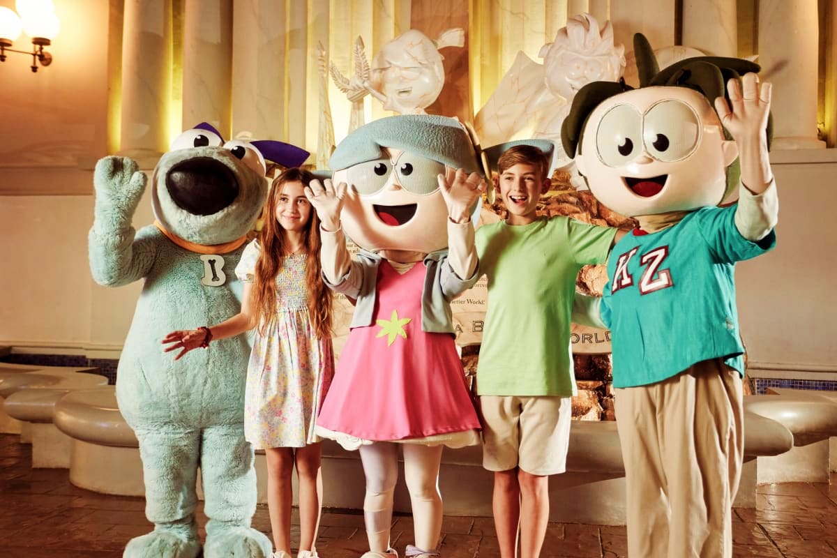 Children posing with cartoon character mascots in elegant indoor theme park setting with classical architecture and marble st