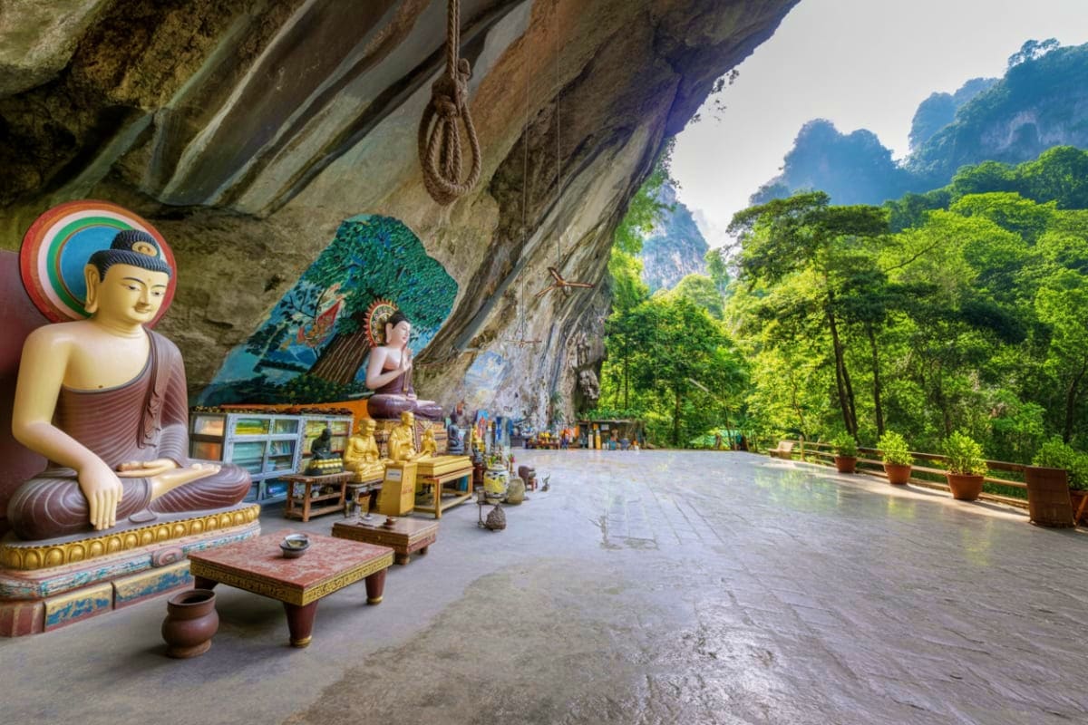 Enroute Krabi city tour to Phuket Buddha statue in cave shrine with limestone cliffs and tropical forest at Khao Luang Cave, Krabi Thailand