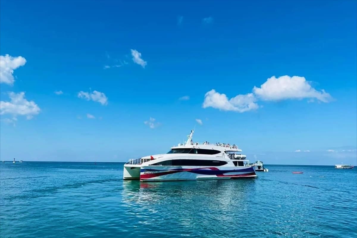 Modern white and red ferry boat anchored in turquoise water under clear blue sky with white clouds