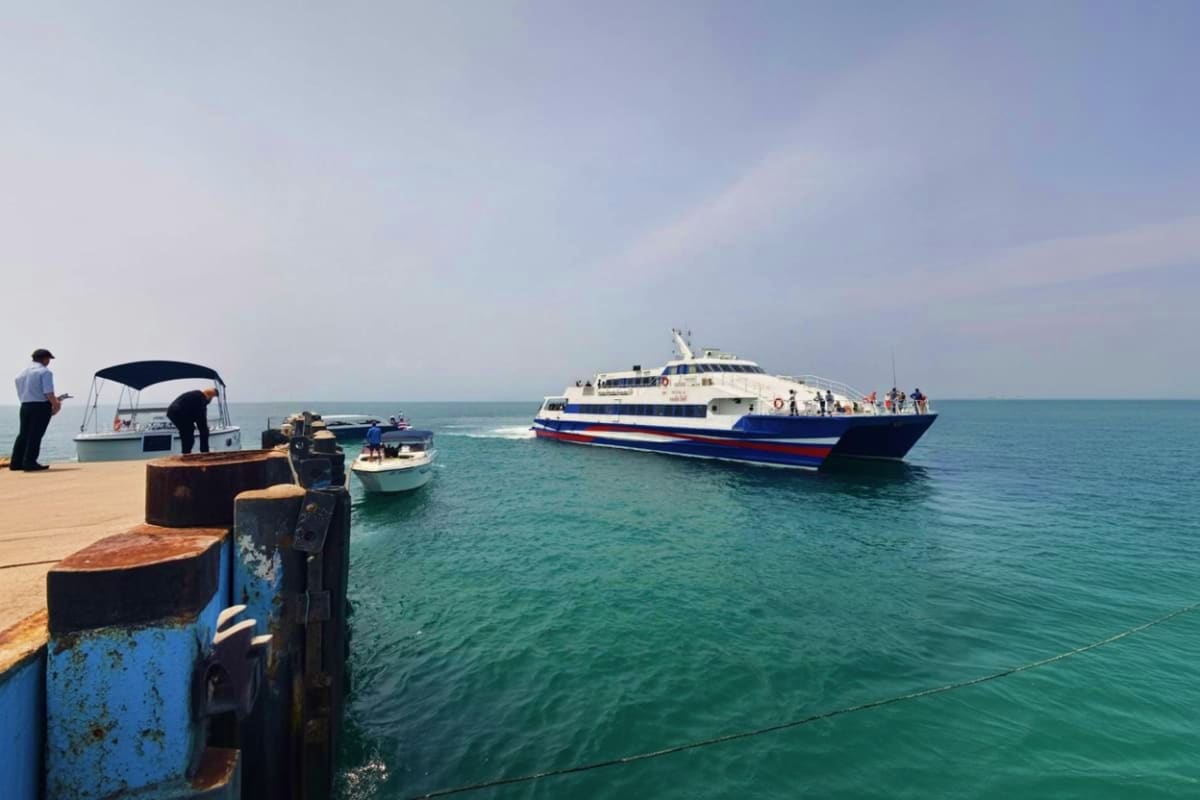 Large blue and white passenger ferry anchored offshore at Koh Samui pier with smaller boats and mooring posts in foreground