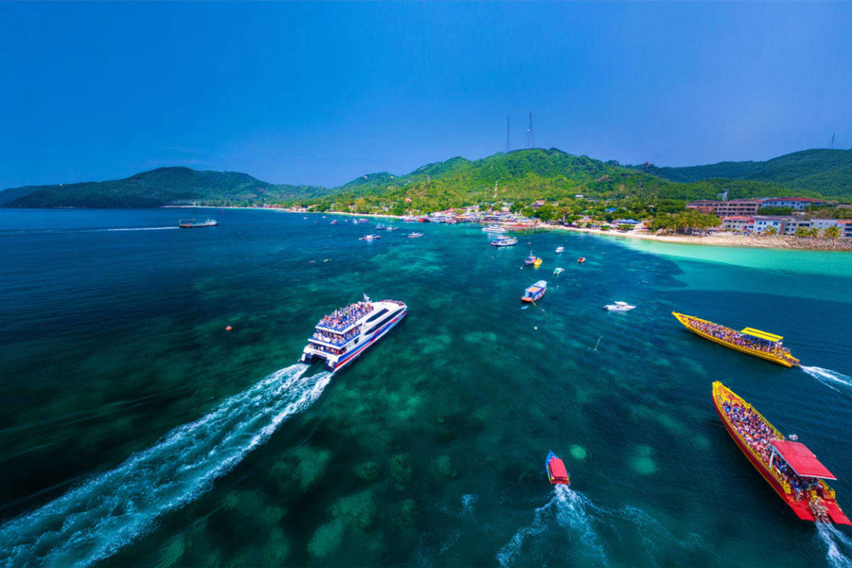 Aerial view of ferry boats and long-tail boats in turquoise waters near Koh Samui with forested hills and beach coastline
