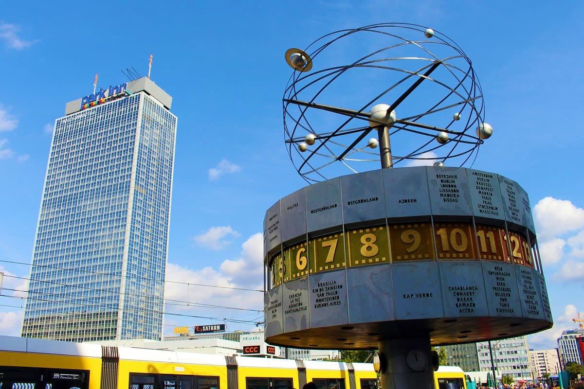 World Clock (Weltzeituhr) at Alexanderplatz in Berlin with yellow public transport train below and modern skyscraper in backg