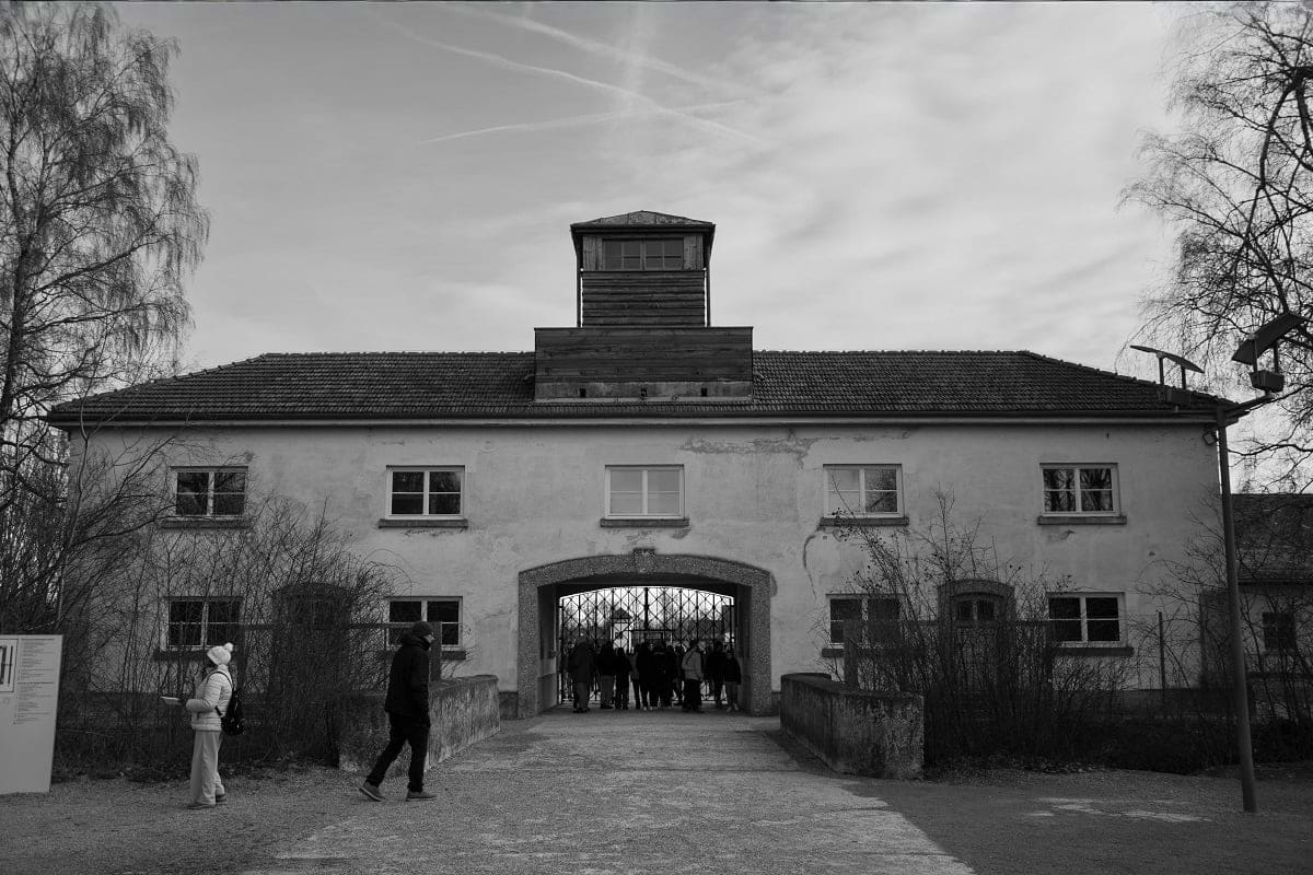 Black and white photograph of Sachsenhausen concentration camp gatehouse with visitors standing in the courtyard, showing the