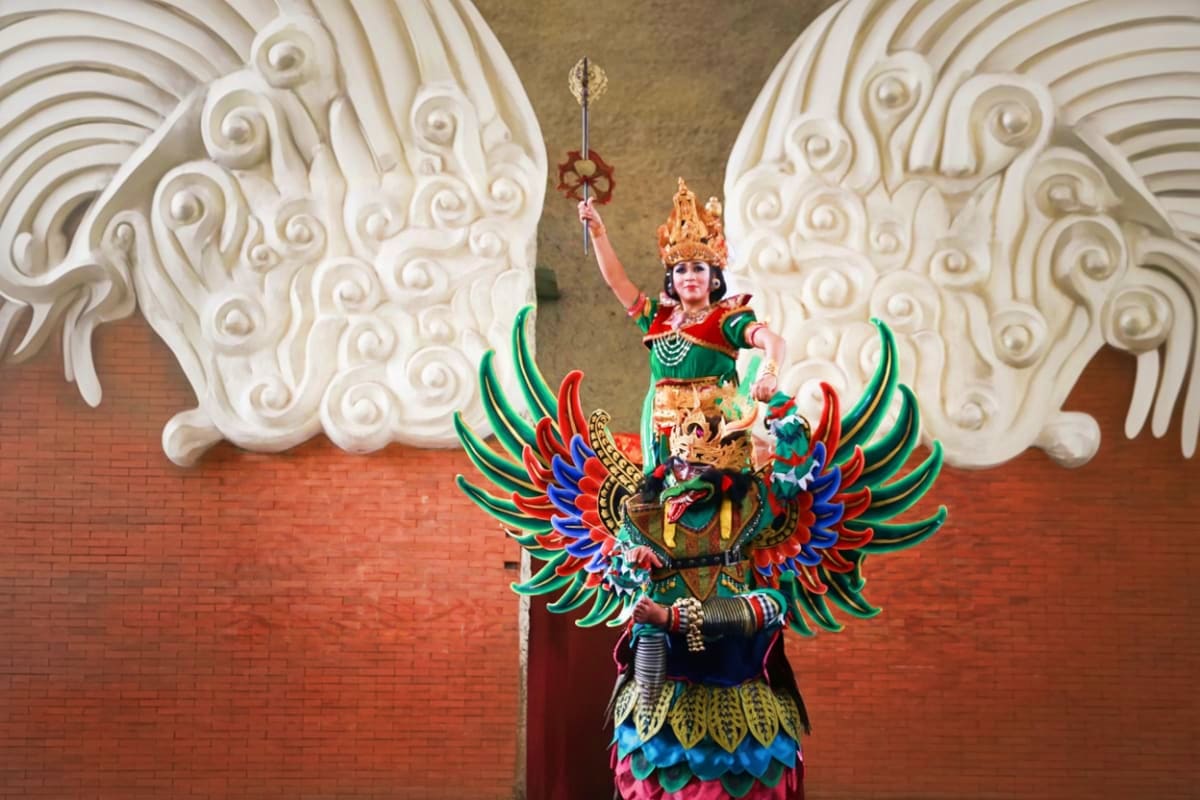 Garuda Wisnu Kencana cultural statue display with deity figure in ornate golden crown and colorful feathered wings against wh