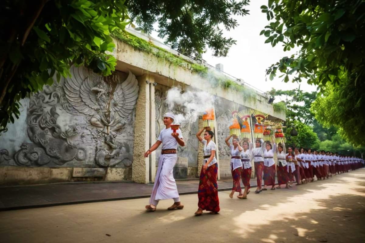 Balinese procession at Garuda Wisnu Kencana cultural park with ornate stone eagle relief and participants in traditional whit