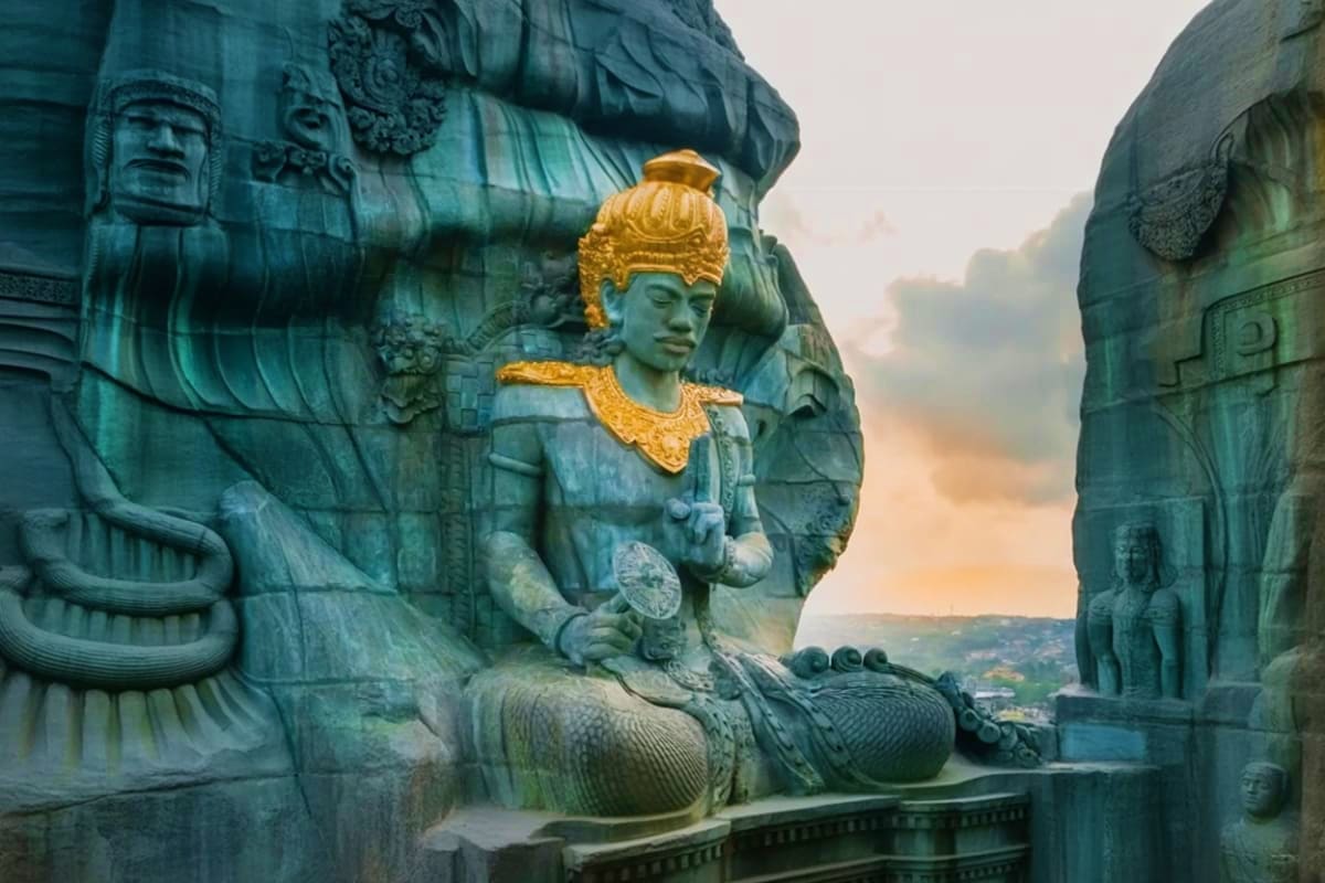 Stone statue of Hindu deity with gold headdress and ornaments at Garuda Wisnu Kencana cultural monument in Bali, Indonesia