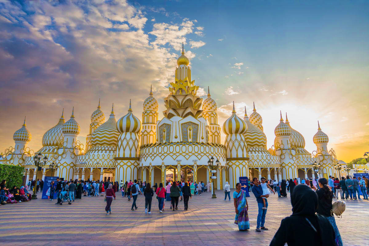 White and gold ornate Russian Orthodox church facade with multiple golden domes at Global Village Dubai, visitors walking in 