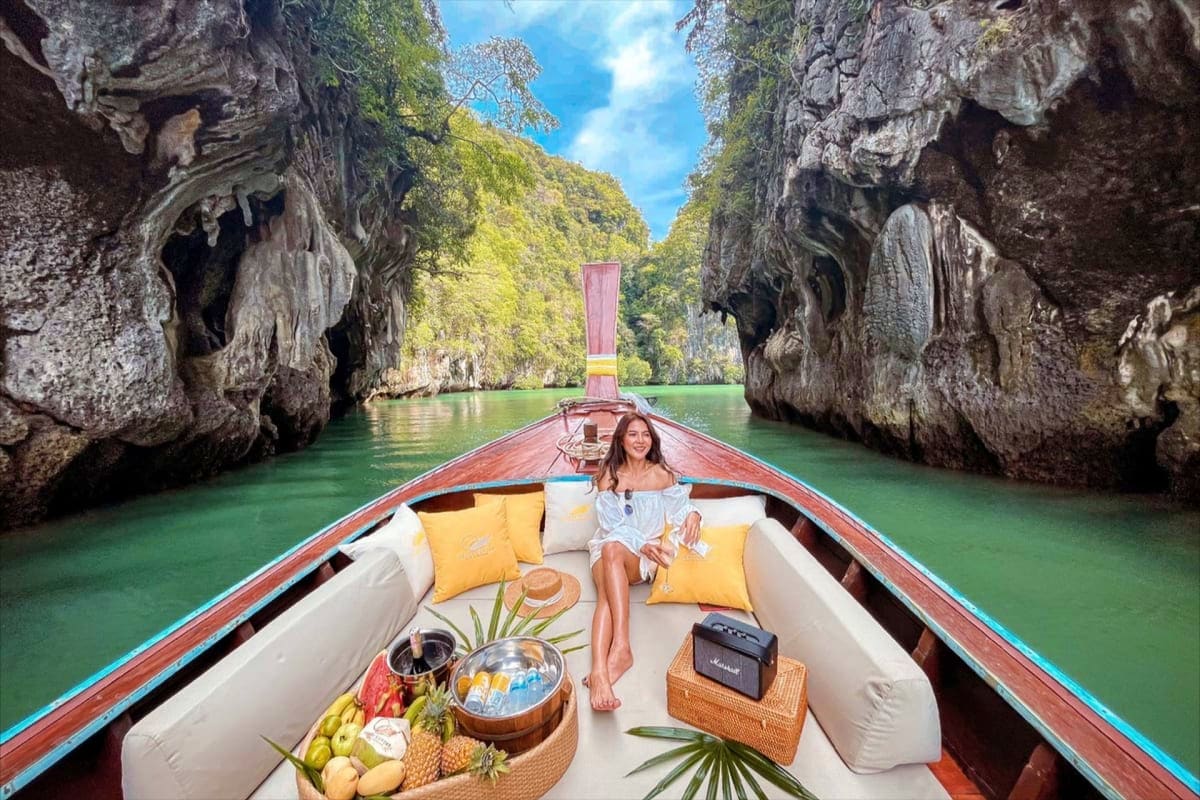 Woman sitting on wooden long tail boat with yellow pillows in emerald water between towering limestone cliffs in Hong Island,