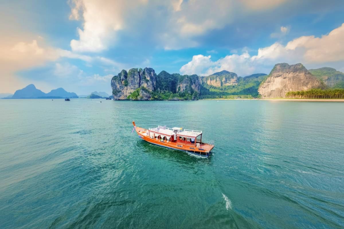 Orange long tail boat on turquoise water with dramatic limestone cliffs and islands in the background under blue sky