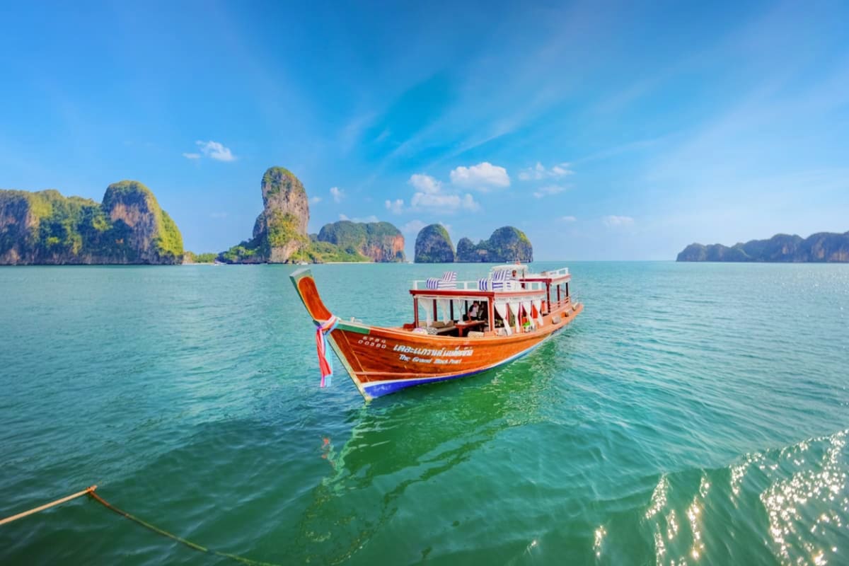 Traditional red and blue longtail boat anchored in turquoise water with limestone karst cliffs in background at Hong Island, 