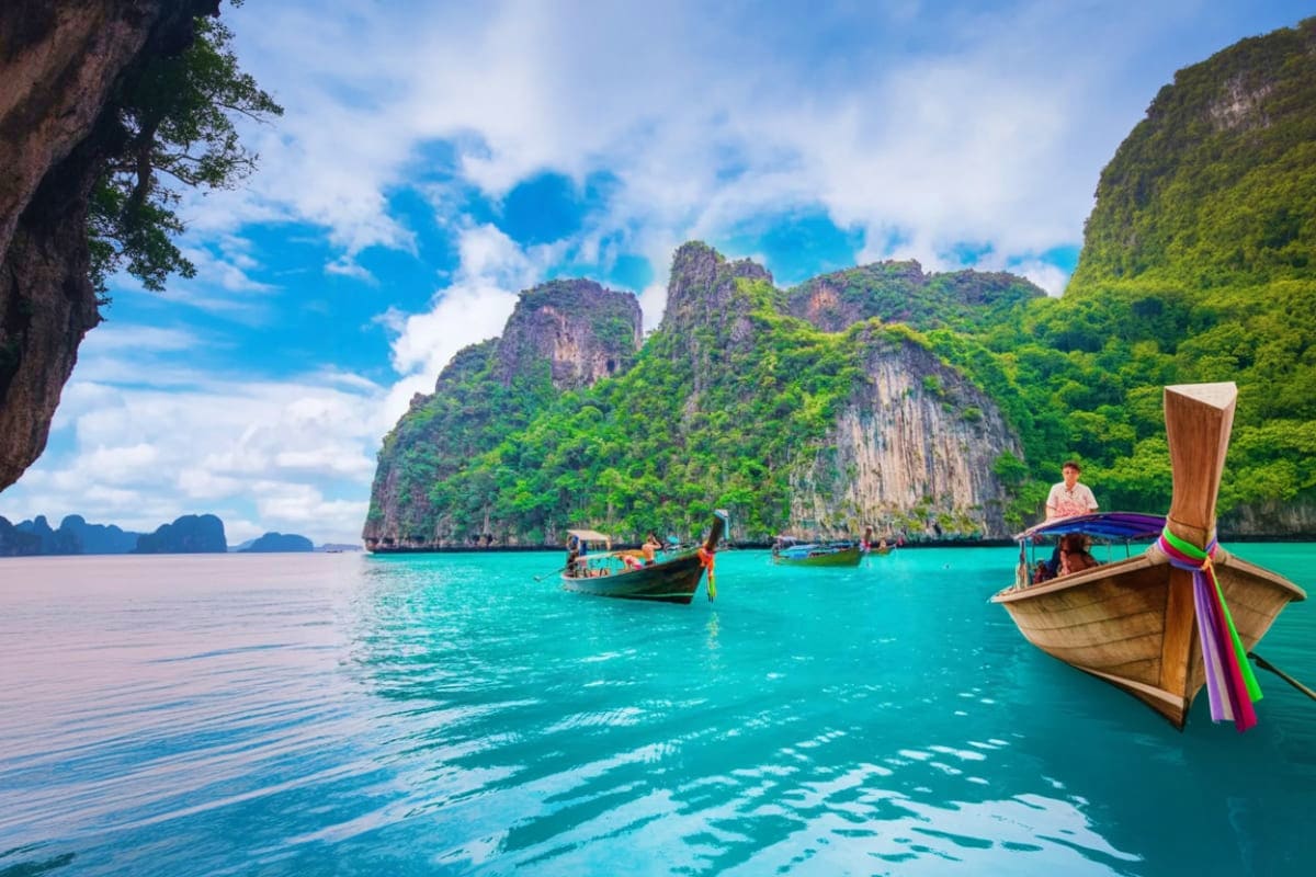 Long tail boats anchored in turquoise water with limestone cliffs at Hong Island, Thailand