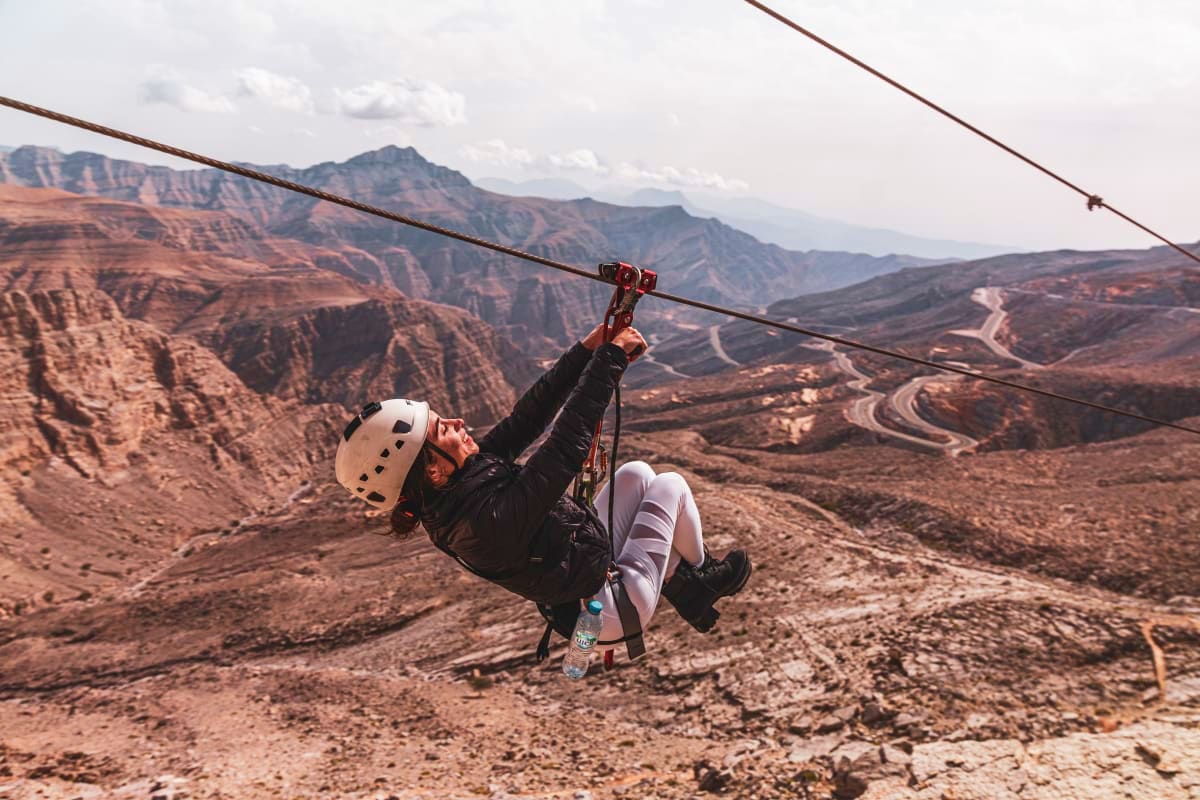 Person ziplining over desert mountains and winding roads at Jebel Jais
