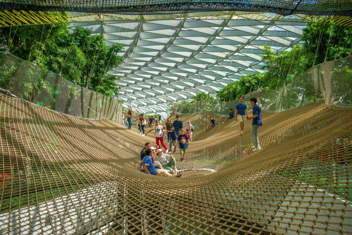 Large indoor net play structure at Jewel Changi Airport with visitors and children climbing and playing on mesh netting under
