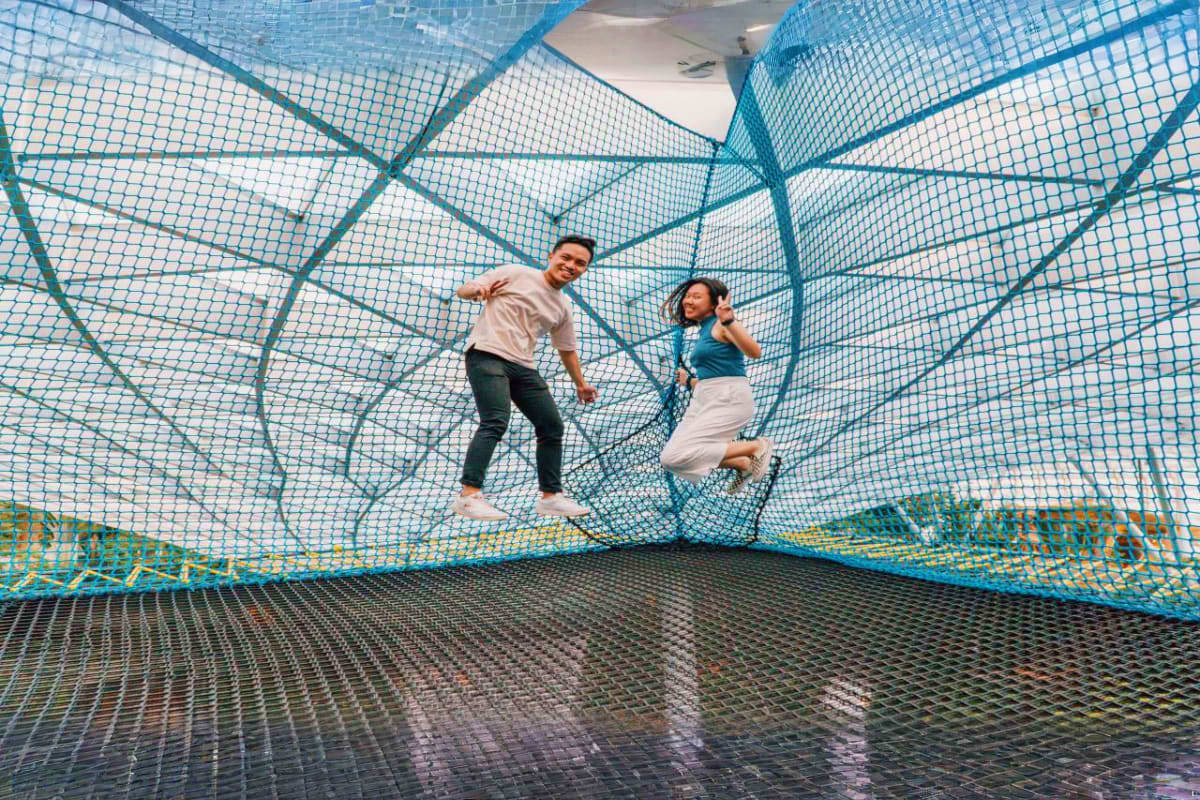 Two people jumping inside a blue mesh trampoline enclosure at an indoor attraction