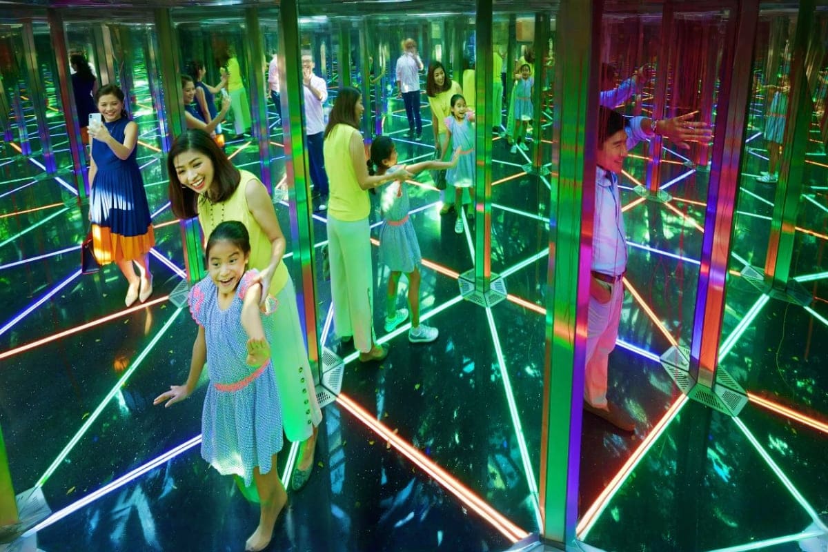 Visitors exploring an interactive mirror maze with neon-lit green and purple glass panels at Jewel Changi Airport