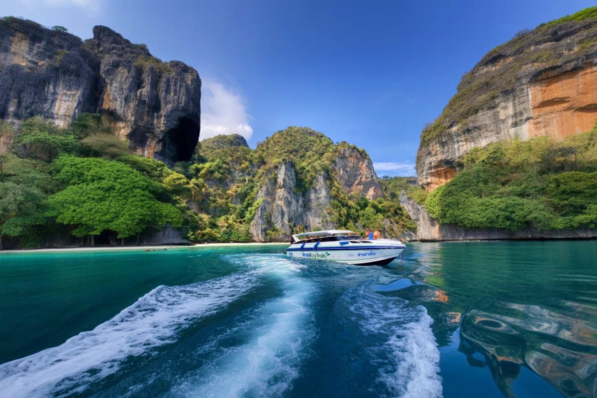 Speedboat anchored in turquoise waters surrounded by towering limestone cliffs and lush jungle vegetation in Krabi, Thailand