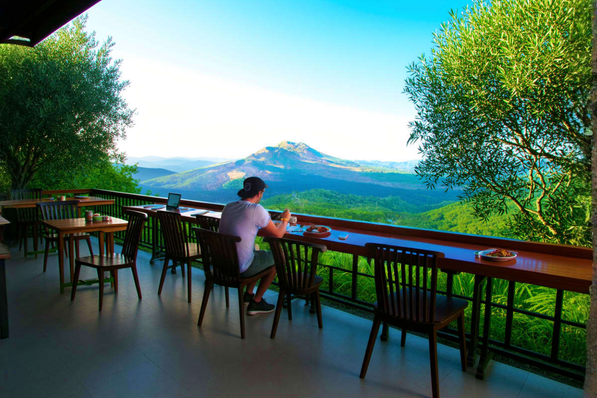 Man dining on mountain terrace overlooking Mount Batur volcano in Kintamani, Bali with lush green valleys below