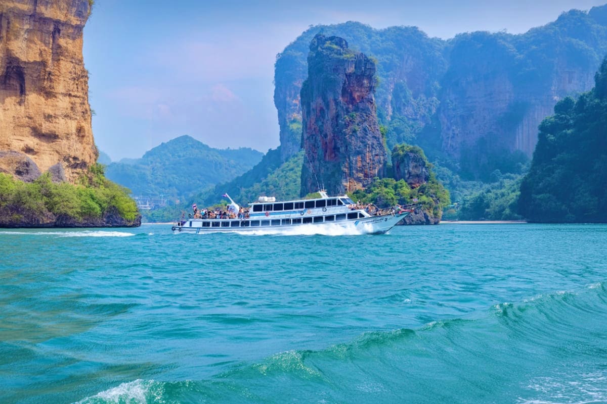 Koh Samui to Surat Thani Ferry Transfers Tourist ferry boat in turquoise waters near dramatic limestone cliffs and karst formations in Thailand