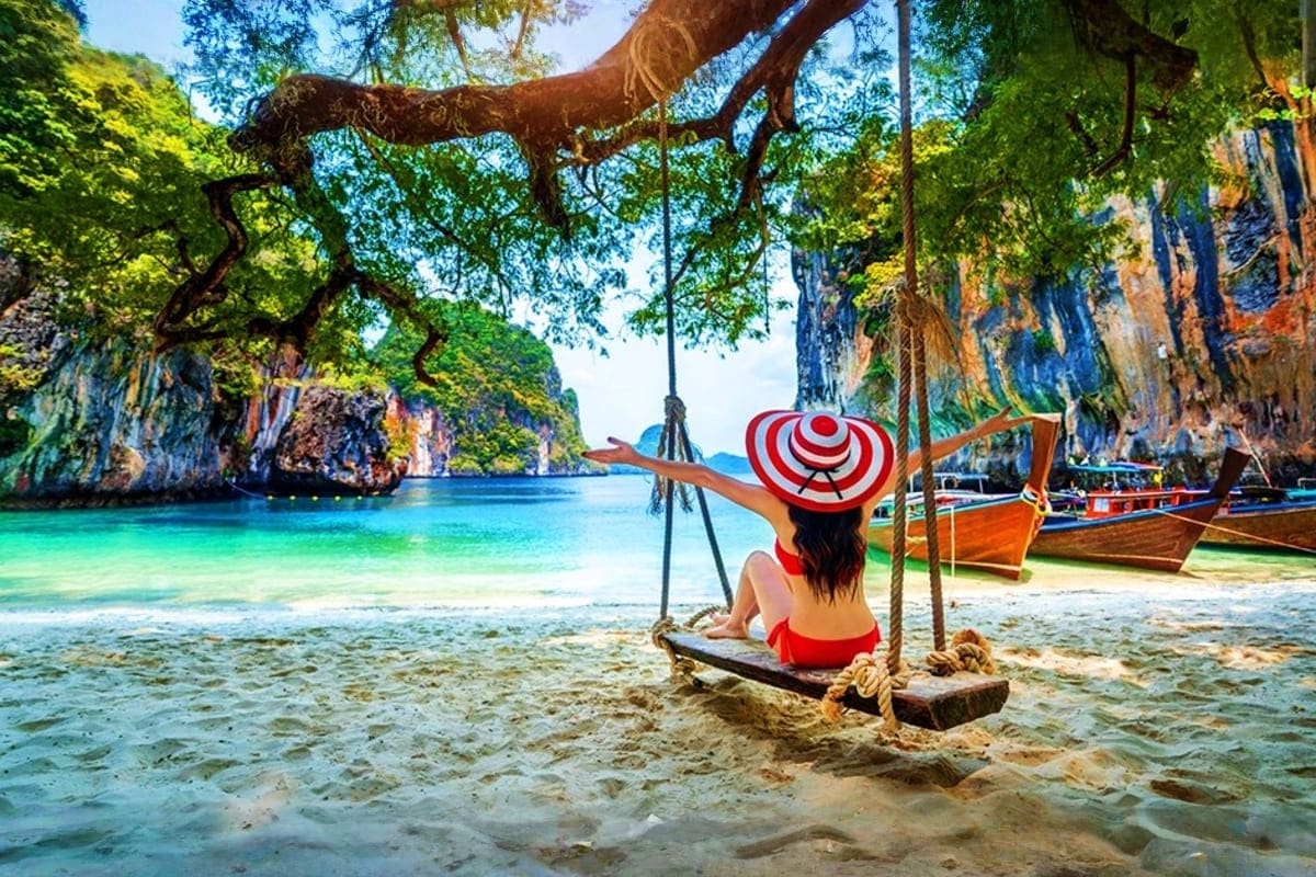 Krabi Island Tour from Phuket Woman on rope swing wearing red and white striped hat overlooking turquoise waters and limestone cliffs in Krabi, Thailand
