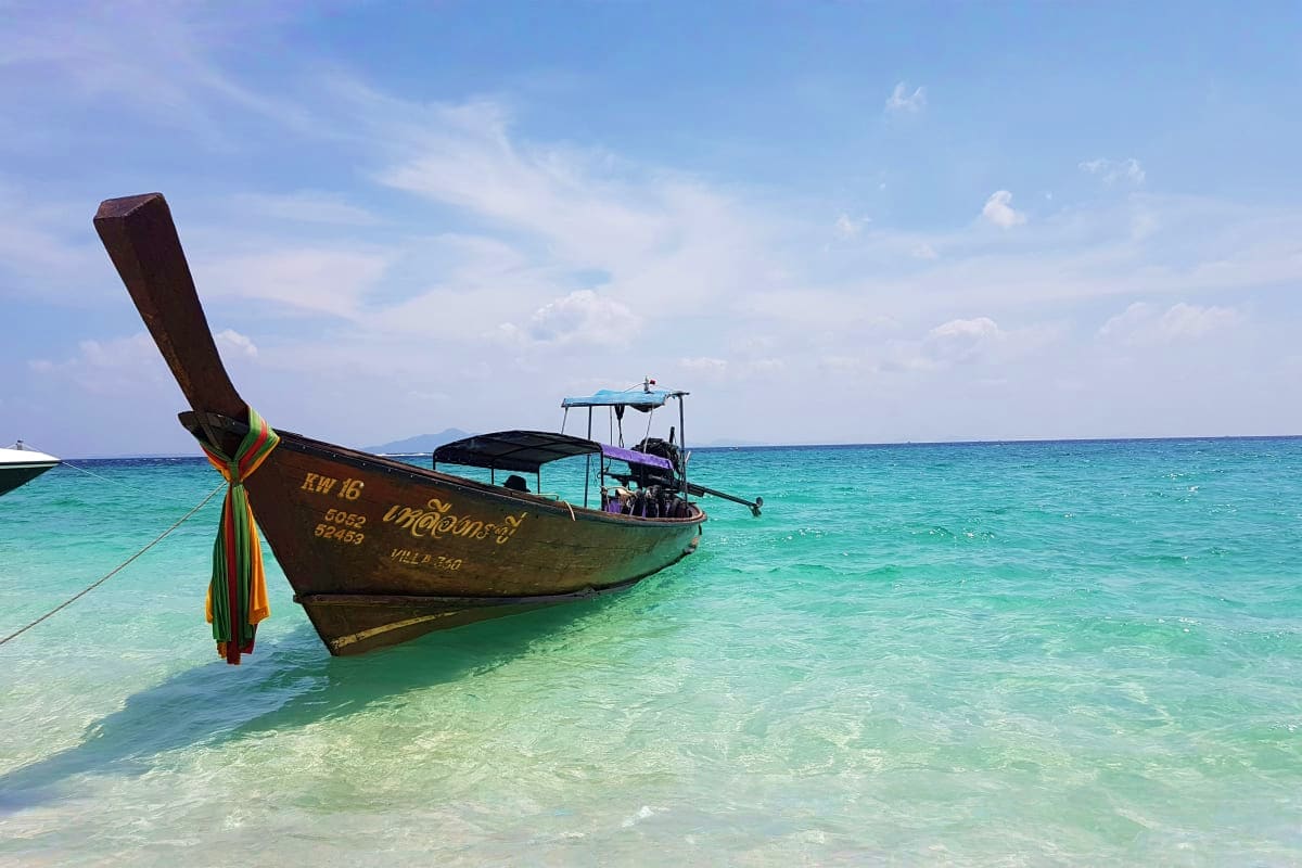 Krabi Island Tour from Phuket Traditional longtail boats anchored in turquoise waters off Krabi Islands with clear blue sky and tropical beach